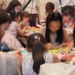 Group of children and adults gathered around tables, crafting with colorful papers and supplies in a classroom setting